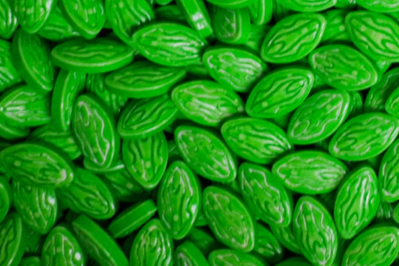 Puede incluir: Primer plano de un mont&oacute;n de caramelos verde brillante. Cada caramelo tiene forma ovalada con una superficie ligeramente texturizada y un dise&ntilde;o blanco en espiral. Los caramelos est&aacute;n dispersos, llenando el marco y creando una exhibici&oacute;n vibrante y llamativa.