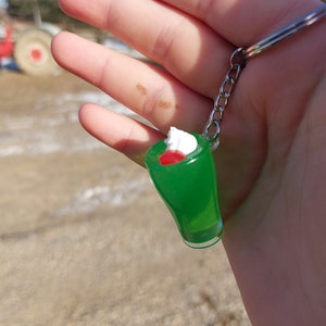 May include: A green and white keychain shaped like a milkshake with a red cherry on top.