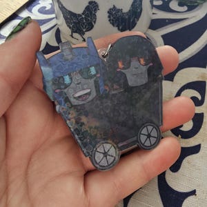 May include: A blue and black cartoon character keychain with wheels. The character has a blue helmet and a black body with a white face. The keychain is attached to a silver ring.