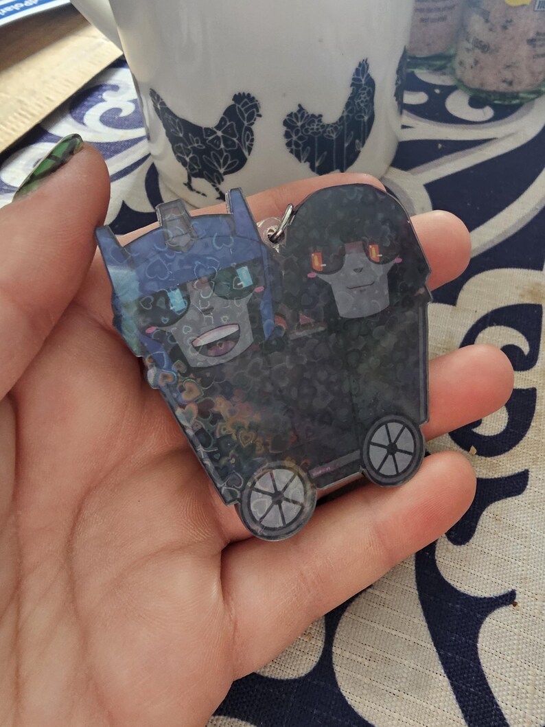 May include: A blue and black cartoon character keychain with wheels. The character has a blue helmet and a black body with a white face. The keychain is attached to a silver ring.