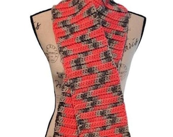 May include: A handmade crochet scarf in a vibrant coral color with alternating stripes of gray and black. The scarf is displayed on a mannequin, showcasing its textured pattern and cozy design. This accessory is perfect for adding warmth and style.
