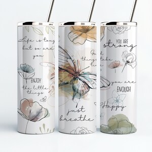 May include: Three stainless steel tumblers with motivational quotes and floral designs. The tumblers feature a butterfly, flowers, and the text "Life is tough but so are you", "Go with the flow, things take time", and "You are strong, you are enough, just breathe, happy".