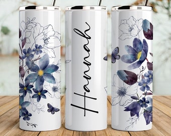 May include: Three stainless steel tumblers with a white background and a floral design in shades of blue and purple. The middle tumbler has the name "Hannah" written in black cursive.