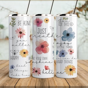 May include: Three stainless steel tumblers with floral designs and inspirational quotes. The tumblers feature quotes like "Be Kind", "Just Breathe", and "You Got This".