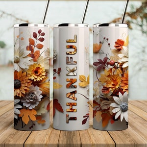 May include: Three stainless steel tumblers with lids and straws. The tumblers are decorated with a floral design featuring white, yellow, and orange flowers and leaves. The middle tumbler has the word "THANKFUL" printed in black letters.