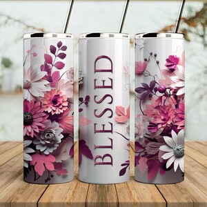May include: Three stainless steel tumblers with a white background and pink and purple floral designs. The center tumbler has the word "BLESSED" printed in pink on the front.