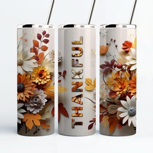 May include: Three stainless steel tumblers with a white background and a floral design in shades of orange, yellow, and white. The center tumbler has the word "THANKFUL" printed vertically in black.