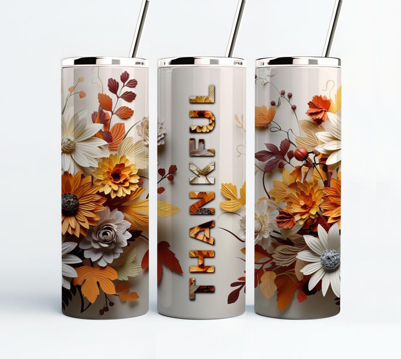 May include: Three stainless steel tumblers with a white background and a floral design in shades of orange, yellow, and white. The center tumbler has the word "THANKFUL" printed vertically in black.