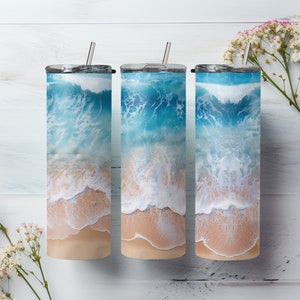 May include: Three stainless steel tumblers with a beach scene design. The tumblers feature a blue ocean with white waves crashing on a sandy beach.