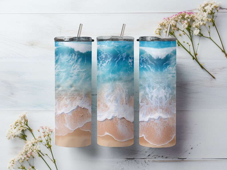 May include: Three stainless steel tumblers with a beach scene design. The tumblers feature a blue ocean with white waves crashing on a sandy beach.