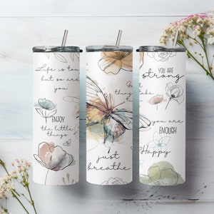 May include: Three stainless steel tumblers with motivational quotes and floral designs. The tumblers feature quotes like "Life is tough, but so are you", "Just breathe", and "You are strong, you are enough".