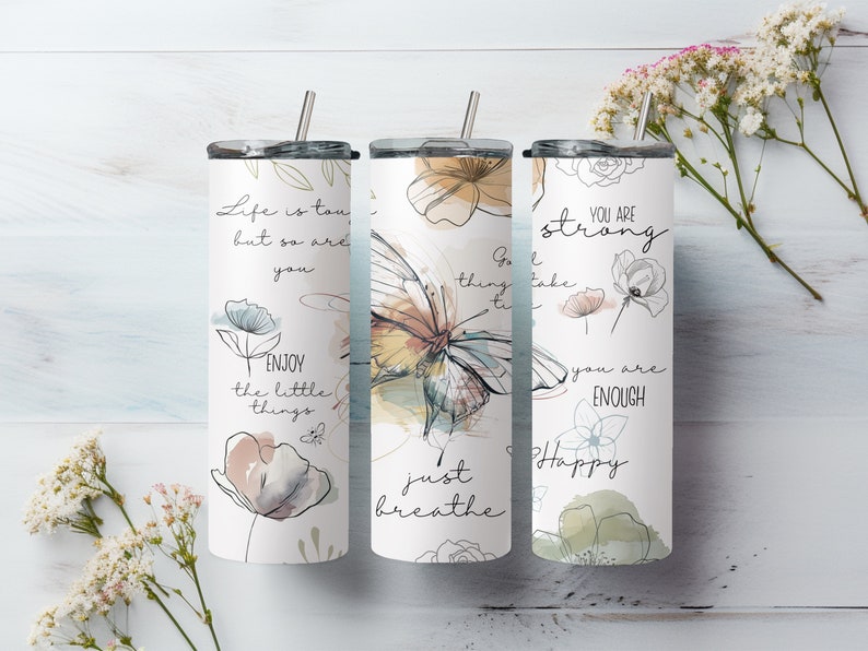 May include: Three stainless steel tumblers with motivational quotes and floral designs. The tumblers feature quotes like "Life is tough, but so are you", "Just breathe", and "You are strong, you are enough".