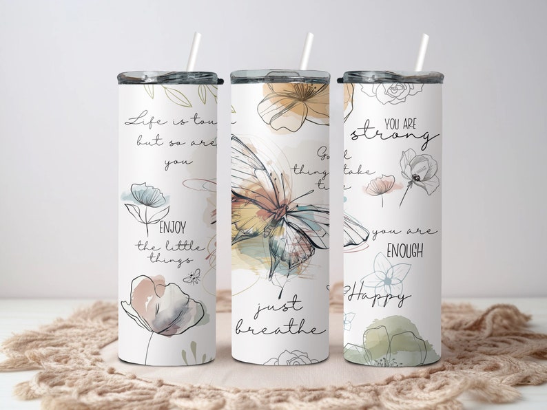 May include: Three stainless steel tumblers with motivational quotes and floral designs. The tumblers feature quotes like "Life is tough, but so are you", "Good things take time", and "You are strong, you are enough".