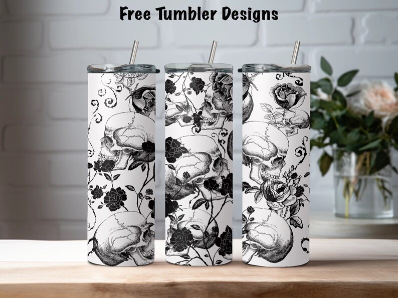 May include: Three stainless steel tumblers with black and white designs featuring skulls and roses. The tumblers are on a wooden surface.