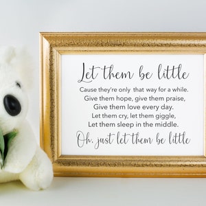 May include: A gold framed print with the text "Let them be little" and a poem about cherishing childhood. The print is sitting on a white surface next to a white stuffed animal.