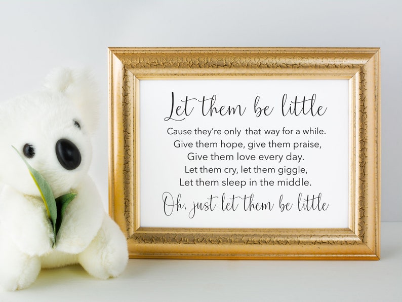 May include: A gold framed print with the text "Let them be little" and a poem about cherishing childhood. The print is sitting on a white surface next to a white stuffed animal.