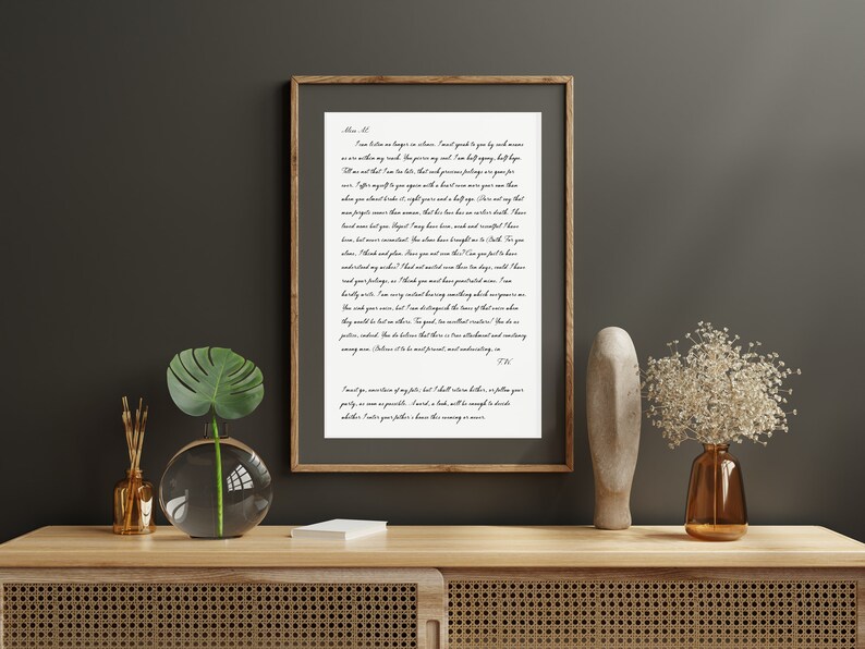 Puede incluir: Una impresi&oacute;n en blanco y negro enmarcada con una carta escrita a mano en letra cursiva. La carta est&aacute; sobre un fondo blanco y est&aacute; enmarcada en un marco de madera marr&oacute;n. La impresi&oacute;n est&aacute; sobre una mesa de madera con un jarr&oacute;n de flores blancas y un jarr&oacute;n de vidrio con una planta verde.