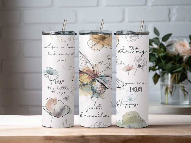May include: Three stainless steel tumblers with motivational quotes and floral designs. The tumblers feature quotes like "Life is tough, but so are you", "Go, thing, take time to breathe", and "You are strong, you are enough, Happy".
