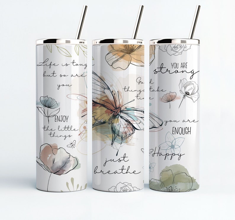 May include: Three stainless steel tumblers with motivational quotes and floral designs. The tumblers feature a butterfly, flowers, and the text "Life is tough but so are you", "Go with the flow, things take time", and "You are strong, you are enough, just breathe, happy".