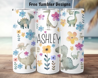May include: Three white tumblers with a dinosaur and floral design. The tumbler in the middle has the name "ASHLEY" printed on it.
