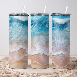 May include: Three stainless steel tumblers with a beach scene design. The tumblers feature a blue ocean with white waves crashing on a sandy beach.