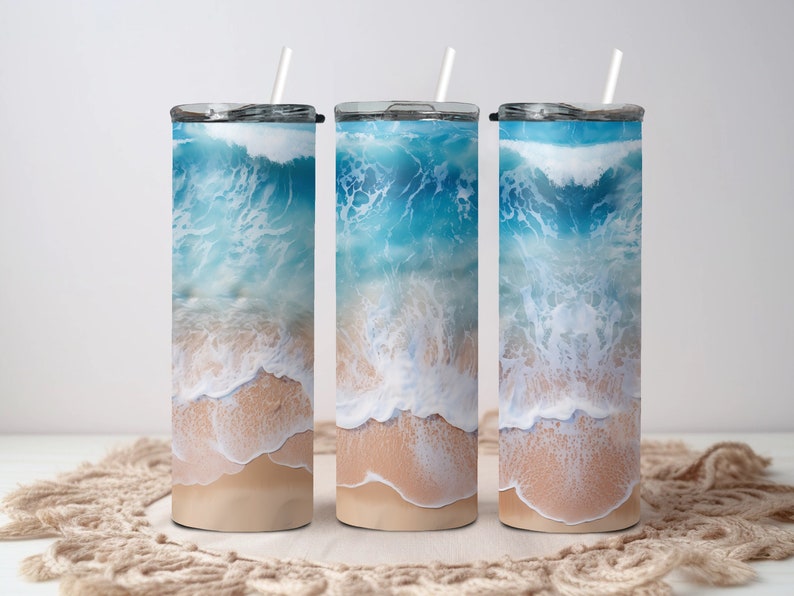 May include: Three stainless steel tumblers with a beach scene design. The tumblers feature a blue ocean with white waves crashing on a sandy beach.