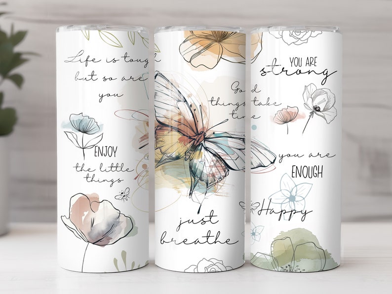 May include: Three white tumblers with inspirational quotes and watercolor floral designs. The quotes are "Life is tough but so are you", "Good things take time, just breathe", and "You are strong, you are enough, Happy".