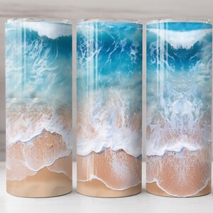May include: Three stainless steel tumblers with a beach scene design. The tumblers feature a blue ocean with white waves crashing on a sandy beach.