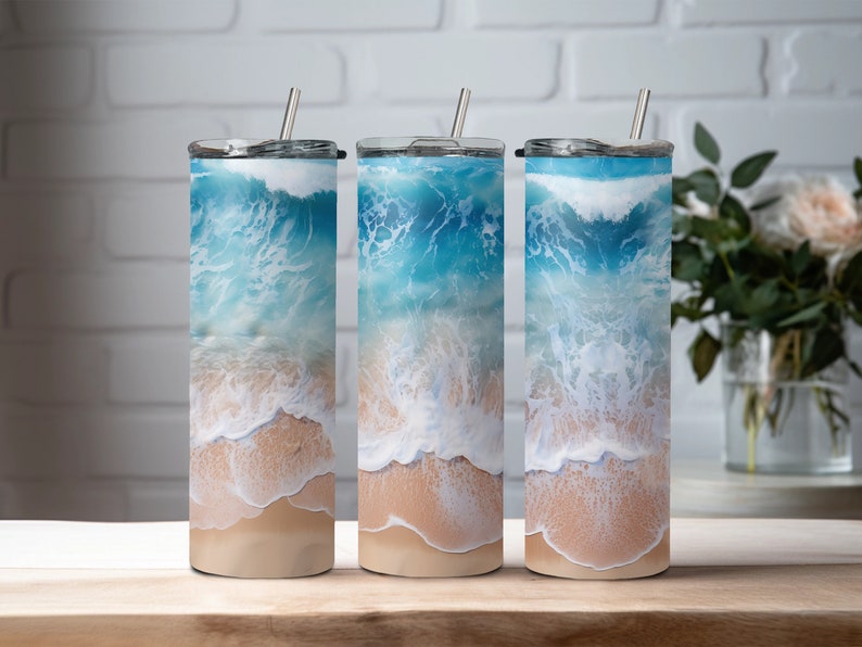 May include: Three stainless steel tumblers with a beach scene design. The tumblers feature a blue ocean with white waves crashing on a sandy beach.