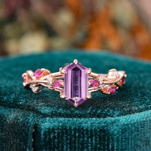 Peut inclure: Une bague en or rose avec une pierre précieuse violette et de petites pierres roses serties dans un délicat motif de vigne.
