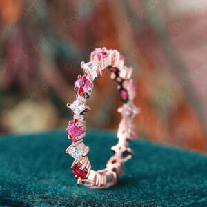 May include: A delicate eternity band ring with alternating square-shaped ruby and diamond stones set in a rose gold band.