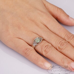 May include: A silver ring with a green stone set in a delicate, leafy design.