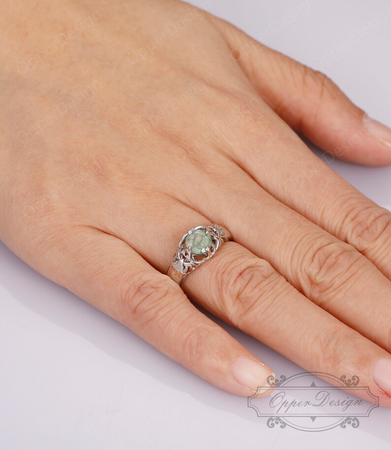 May include: A silver ring with a green stone set in a delicate, leafy design.