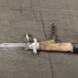 May include: A vintage pocket knife with a wooden handle covered in brown fur. The blade is open and the knife has a corkscrew.