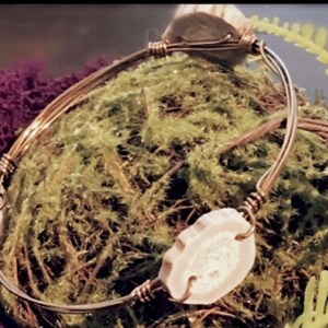 May include: A copper wire bracelet with three antler slices attached. The bracelet is on a bed of green moss.