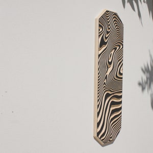 May include: A black and white abstract wood wall art piece with a wavy pattern. The art is mounted on a white wall.