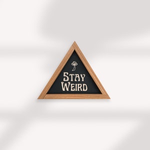 May include: A triangular wooden frame with a black chalkboard insert. The chalkboard has a white mushroom graphic and the text "Stay Weird" in a retro font.