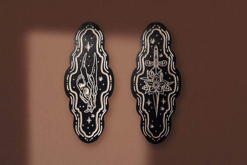 May include: Two black wooden plaques with gold-colored designs. The plaque on the left features a stylized skull and bones, while the plaque on the right features a dagger and a flower.