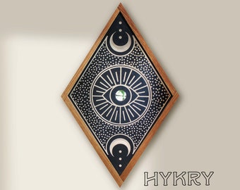 May include: A diamond-shaped wooden frame with a black and white design featuring a stylized eye with a mirrored pupil, surrounded by a circle of rays and a dotted background. The frame also includes two crescent moons and three dots.