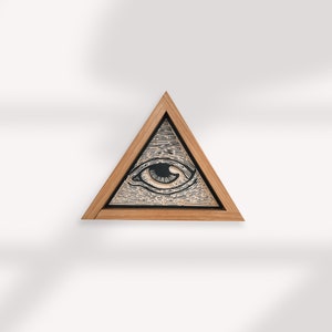 May include: A wooden framed triangle with an all-seeing eye design inside. The eye is black with a white iris and pupil. The triangle is a light brown wood.