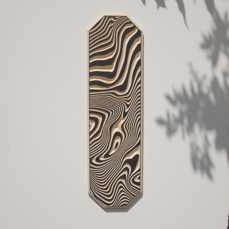 May include: A black and white abstract wood wall art piece with a wavy, flowing pattern. The piece is shaped like a long, narrow rectangle with rounded corners.