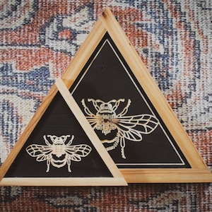 Peut inclure: Deux cadres triangulaires en bois avec des fonds noirs et des motifs d'abeilles blanches complexes. Le cadre le plus petit est &agrave; l'int&eacute;rieur du cadre le plus grand.