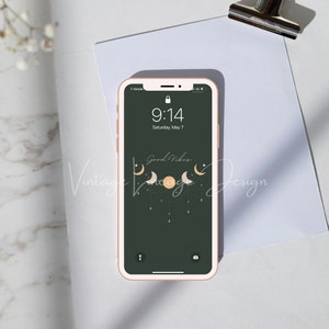 Op de afbeelding: Een smartphone met een roze hoesje toont een donkergroene achtergrond met een hemels ontwerp van manen en een zon. Het scherm toont de tijd als 9:14 uur, zaterdag 7 mei. De woorden "Good Vibes" zijn ook zichtbaar.