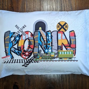May include: A white pillowcase with a colorful train design featuring the name "Ronin" in a graffiti style. The design includes a train tunnel, railroad crossing sign, and train tracks.
