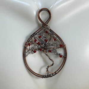 May include: A copper wire tree of life pendant with red beads for leaves. The pendant is on a white background.