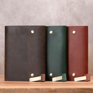 Peut inclure: Trois journaux reliés en cuir de couleur marron, vert et rouge, chacun avec une fermeture en métal doré.