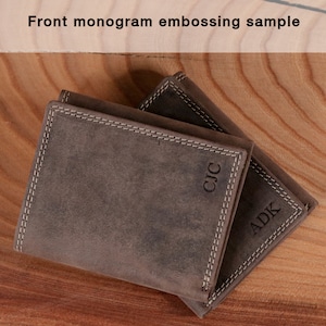 May include: Two brown leather wallets with white stitching and embossed initials. The wallets are stacked on a wooden surface. The top wallet has the initials "CJC" and the bottom wallet has the initials "ADK". The text "Front monogram embossing sample" is at the top.