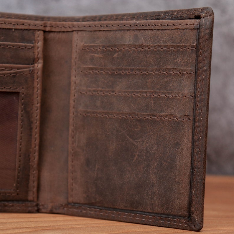 May include: Open view of a brown leather wallet. The wallet has multiple card slots and a clear ID window. The leather has a distressed look with visible stitching around the edges and compartments. The wallet is open, revealing its interior.