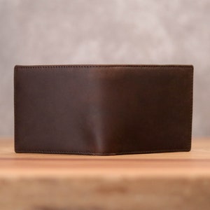 Puede incluir: Una cartera de cuero marr&oacute;n con un dise&ntilde;o sencillo. La cartera est&aacute; cerrada y tiene una superficie lisa.