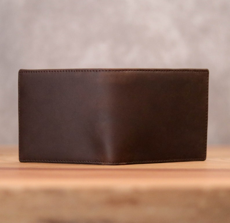 Puede incluir: Una cartera de cuero marr&oacute;n con un dise&ntilde;o sencillo. La cartera est&aacute; cerrada y tiene una superficie lisa.